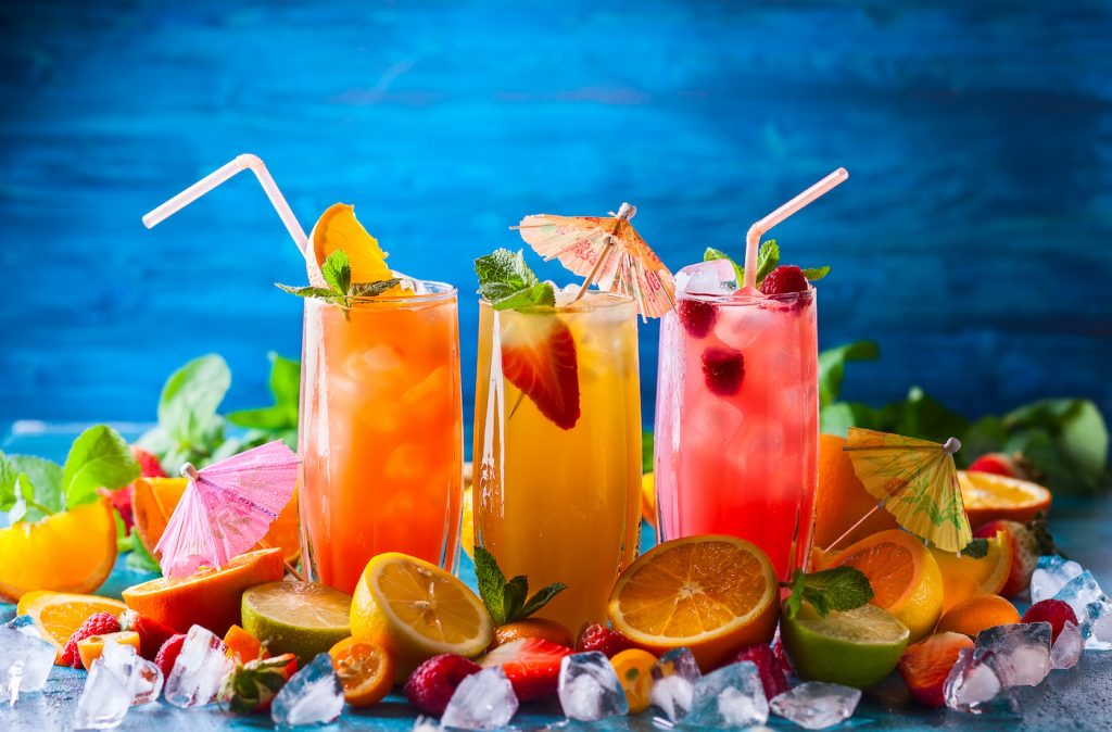 Different types of summer drinks in glasses, cubes of ice and slice of fruits  on blue table. Health